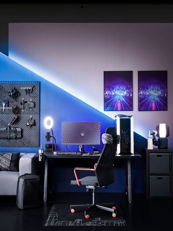 Ett gamingrum med svart golv och vita väggar upplyst i blått och inrett med svart gamingbord och gamingstol.