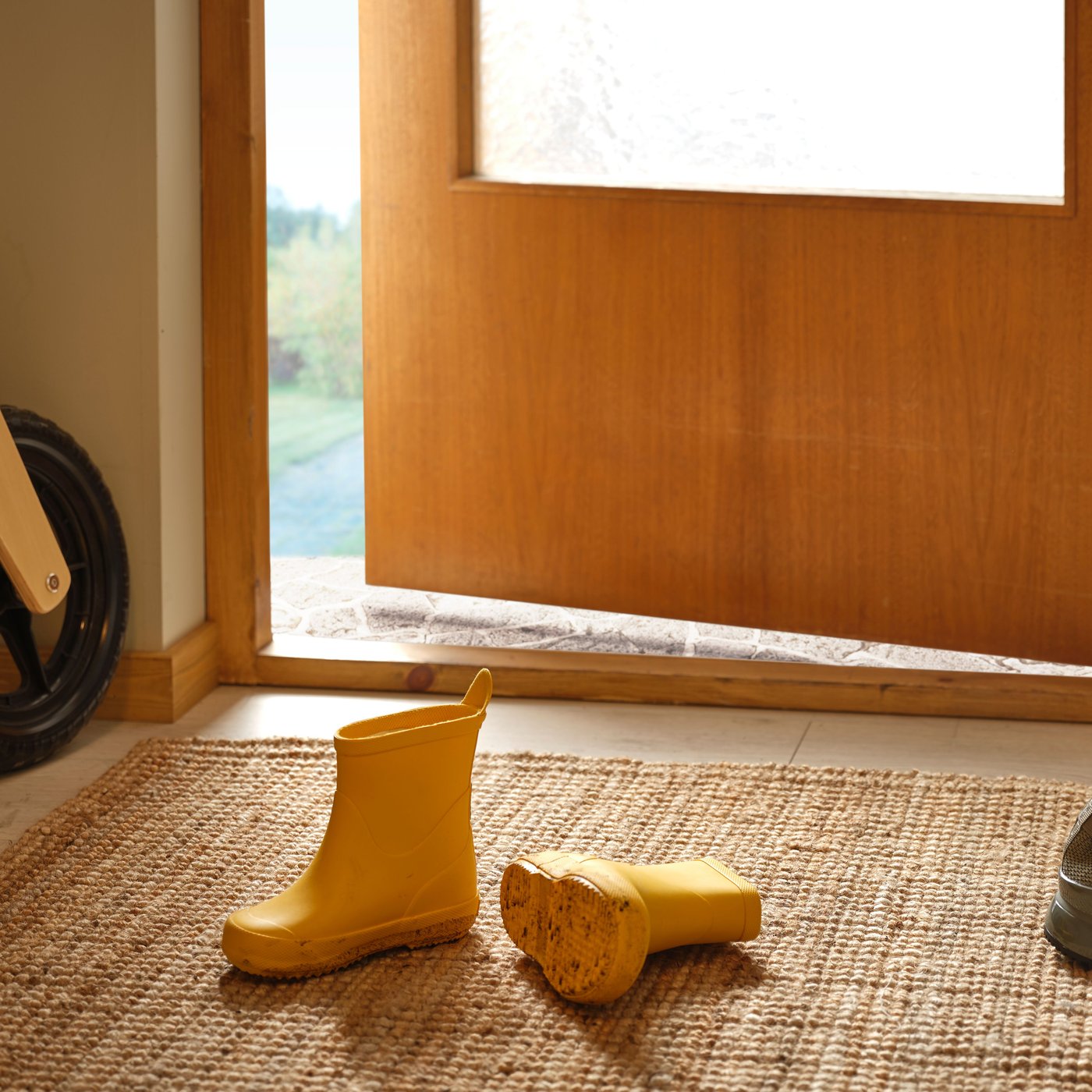 A pair of yellow children's rain boots on a woven doormat in front of an open door, creating an inviting and homely scene.