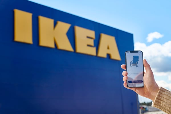 Hand holding up a mobile phone featuring IKEA product against an IKEA store in the background