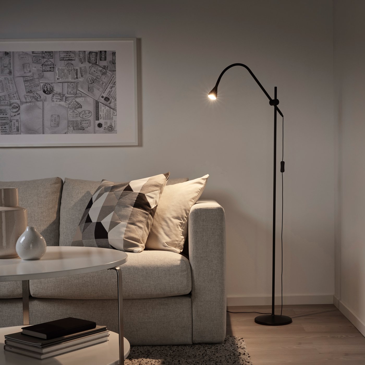 Lampada da terra/lettura a LED NÄVLINGE nera in un angolo del soggiorno. La luce è orientata su un divano grigio con cuscini - IKEA.