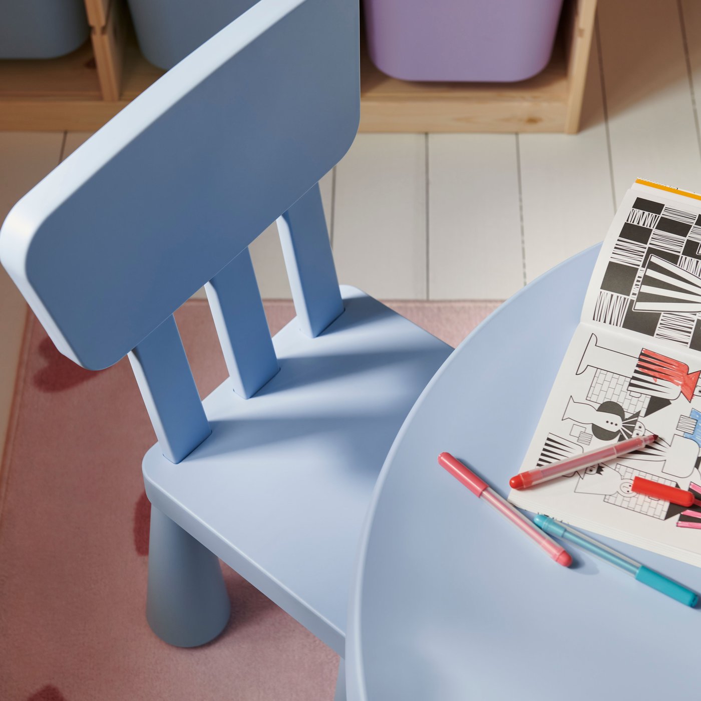 A light blue children’s chair in front of a children’s table, both from the MAMMUT range. A colouring book is on the table.