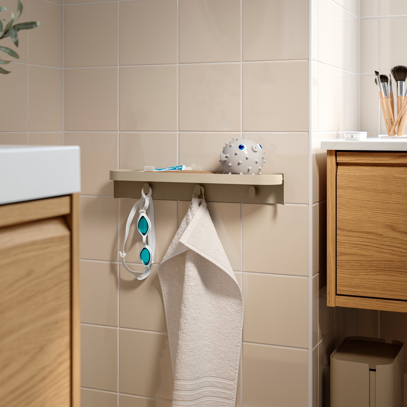 A blowfish toy is on top of a grey-beige FLORSJÖN wall shelf with three hooks, at wash-basin level on a tiled bathroom wall.