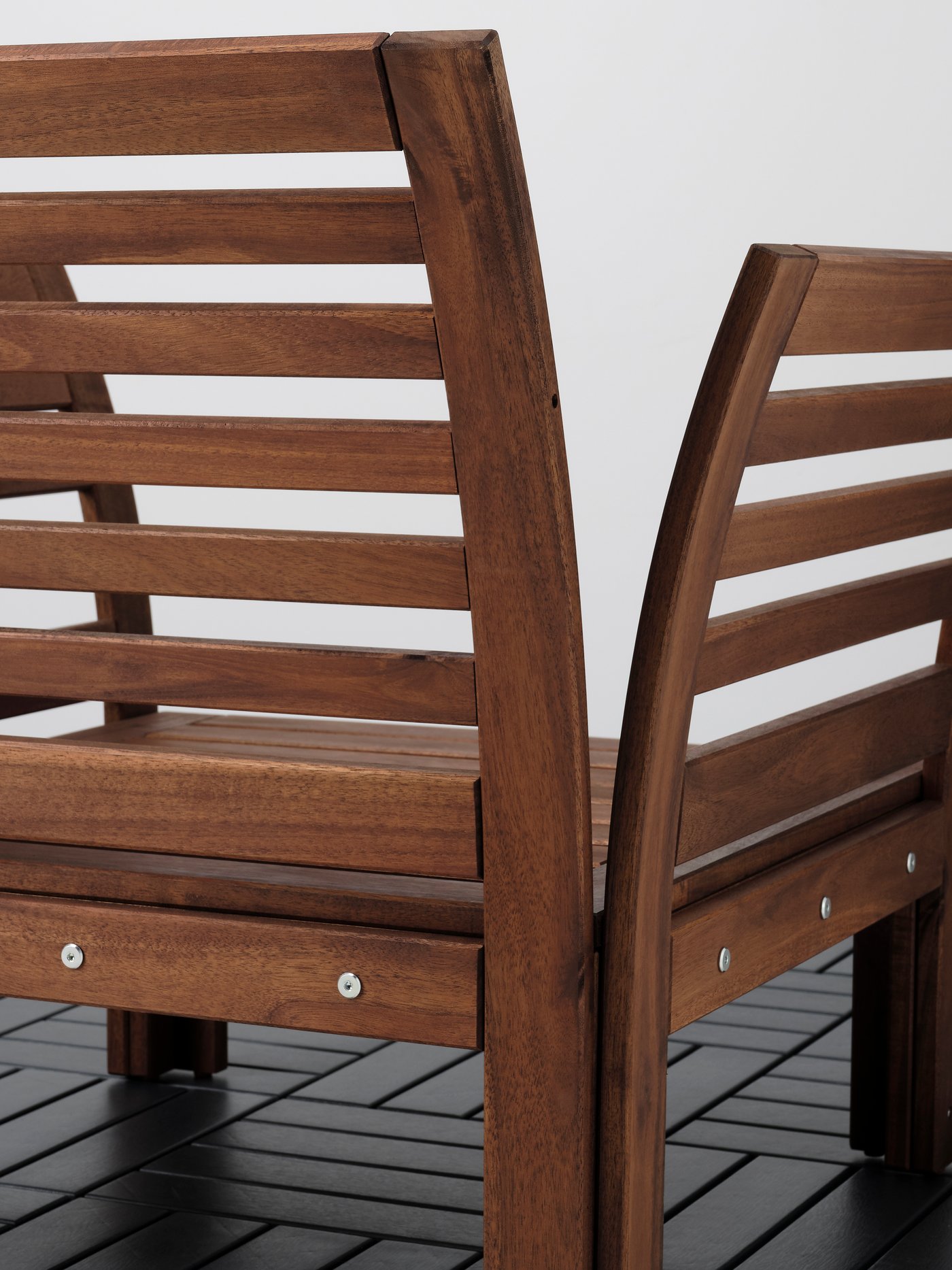 The back side of an ÄPPLARÖ outdoor armchair standing on a floor clad in shiny, black rectangular tiles.