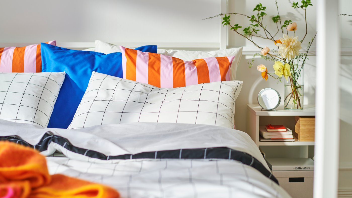 Close-up of bed with a lot of pillows in different patterns and colours. Bedside table on the right.