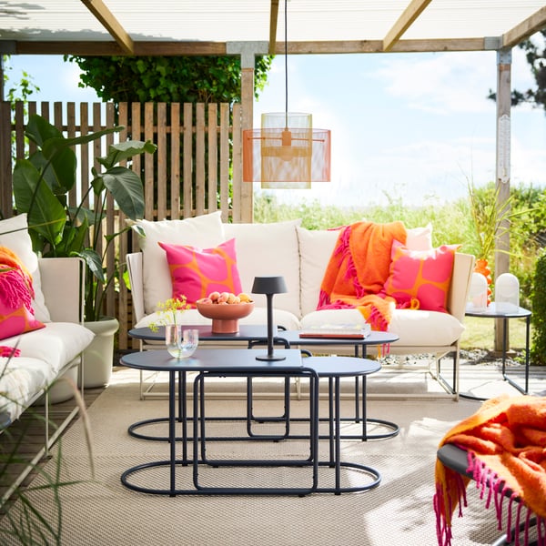An oudoor lounge area under a roof top terrace featuring black-blue GRYTSHOLM nest of tables with fruits and decorations. 