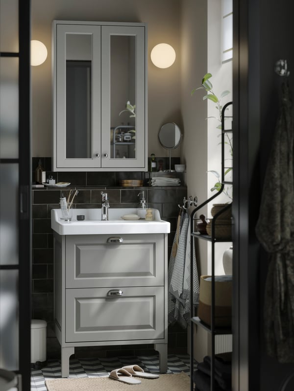 Un pequeño baño de estilo tradicional con muebles TÄNNFORSEN de almacenaje en gris claro, lámparas redondas y detalles en negro.