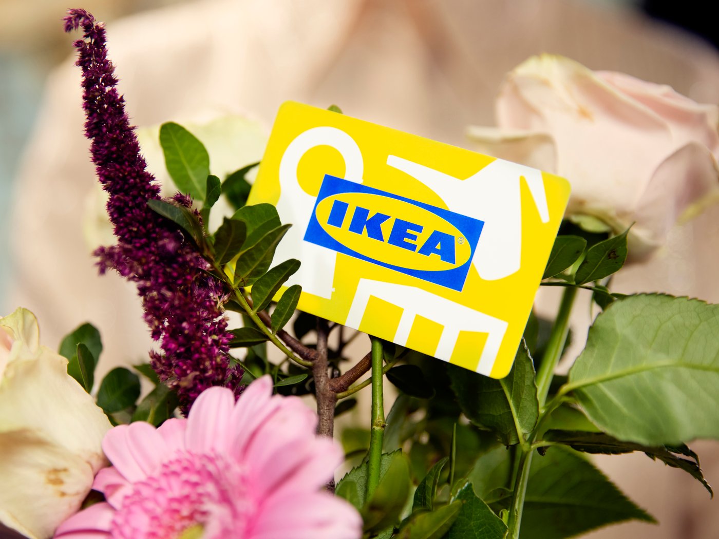 Žuta IKEA poklon-kartica umetnuta je među buket cveća s ružičastom gerberom, belim ružama i zelenim lišćem.