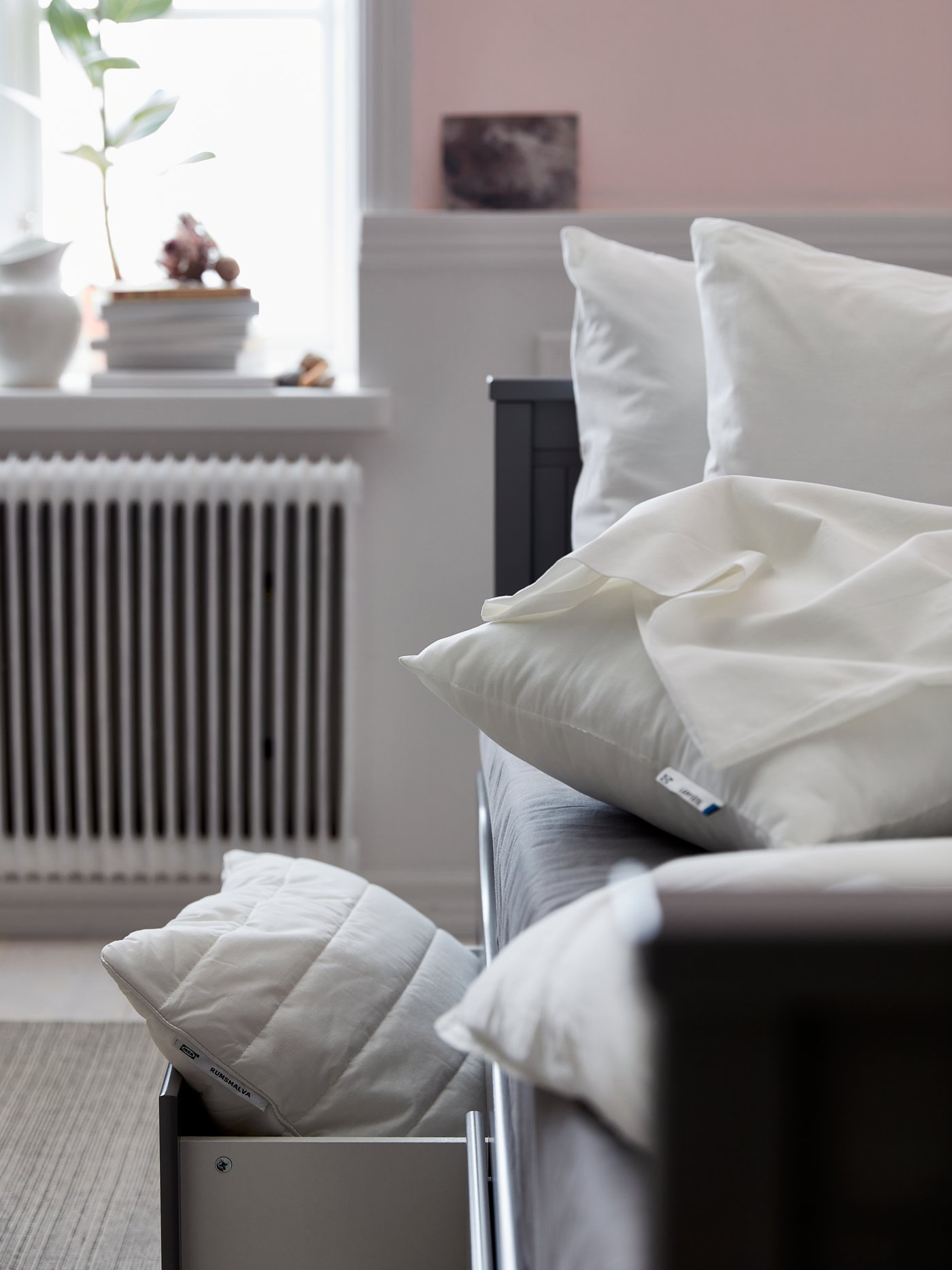 Una cama con almacenaje donde se ve una almohada RUMSMALVA dentro de un cajón de la cama y otras almohadas sobre la cama.