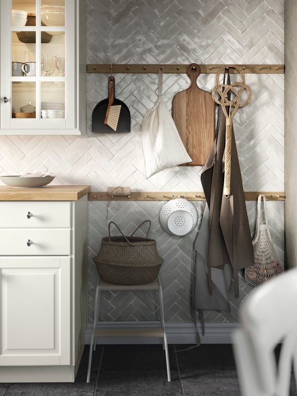Two rails with hooks hang on a wall in a kitchen, alongside a kitchen apron, a chopping board and a carpet beater