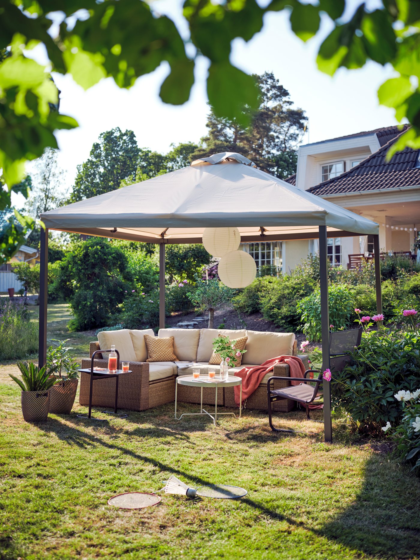 A SOLLERÖN corner outdoor sofa with beige cushions and a black armchair under a HIMMELSÖ gazebo on a sunny garden lawn.