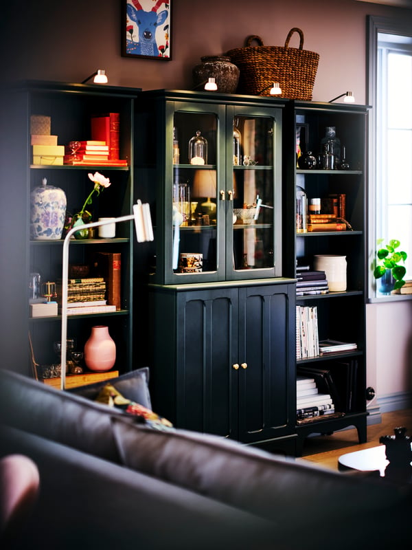 A dark blue-green LOMMARP cabinet with glass doors flanked by two LOMMARP bookshelves, all filled with books and ornaments.
