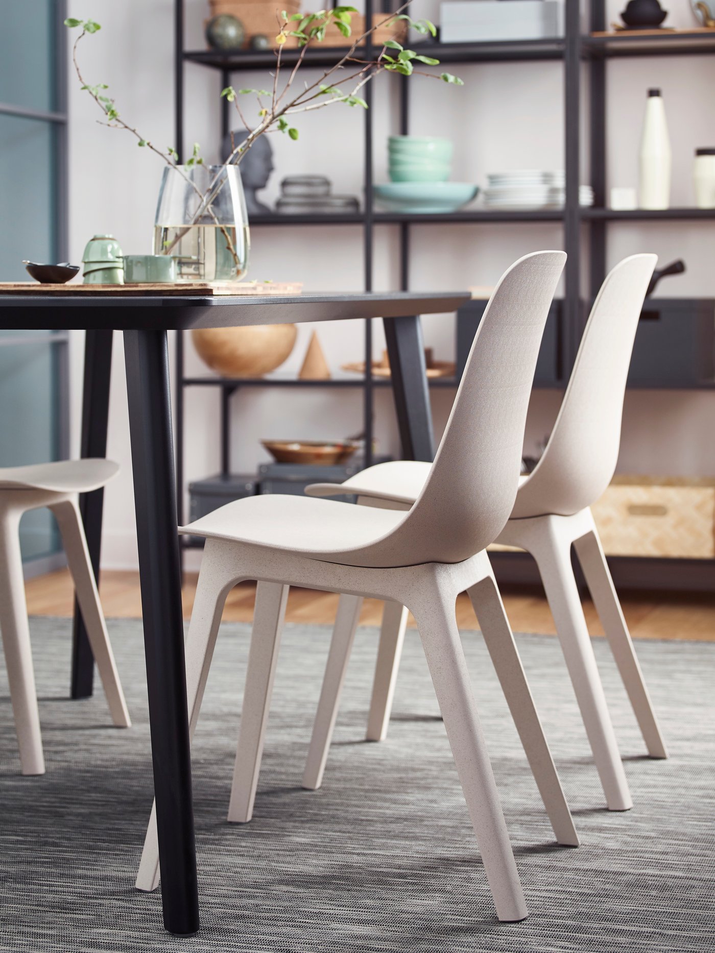 A grey/black HODDE rug flatwoven, in/outdoor in the dining room with ODGER chairs on top next to a dining table.