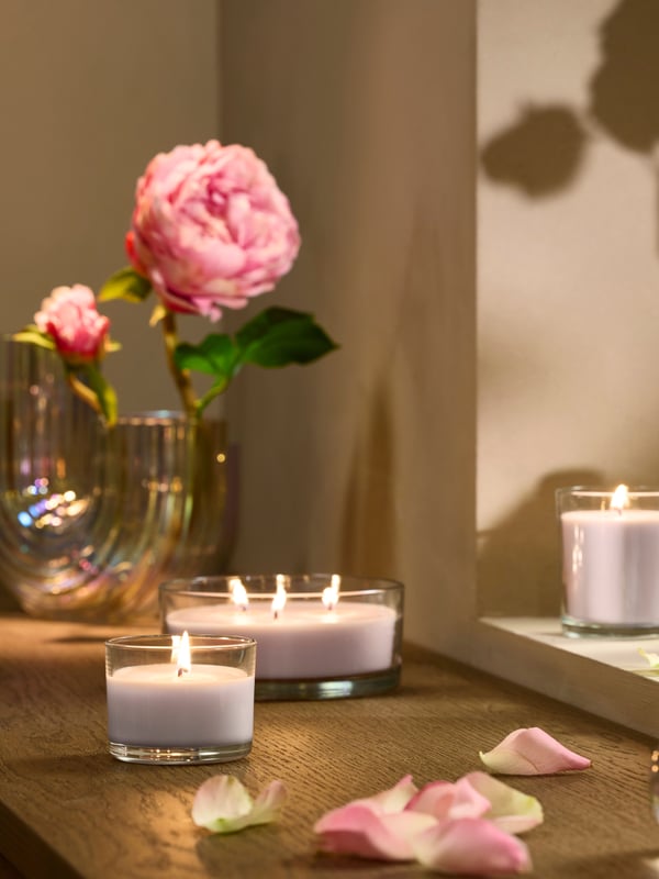 Vela aromática LOTSFÅGEL en vaso, con flores de color rosa pálido.