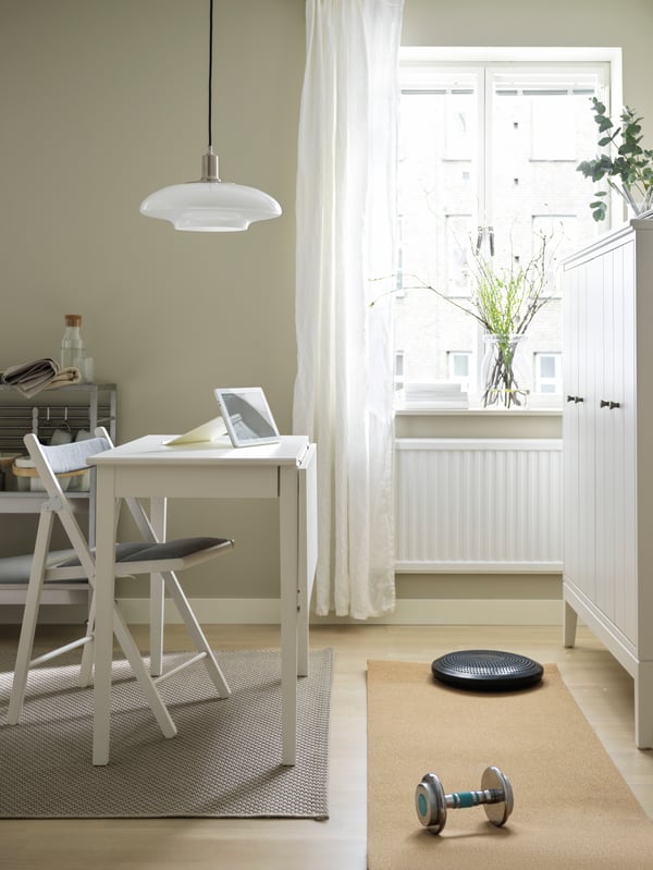 A yoga mat and weights placed between a TERJE chair and a white drop-leaf table combo, and a white IDANÄS cabinet.