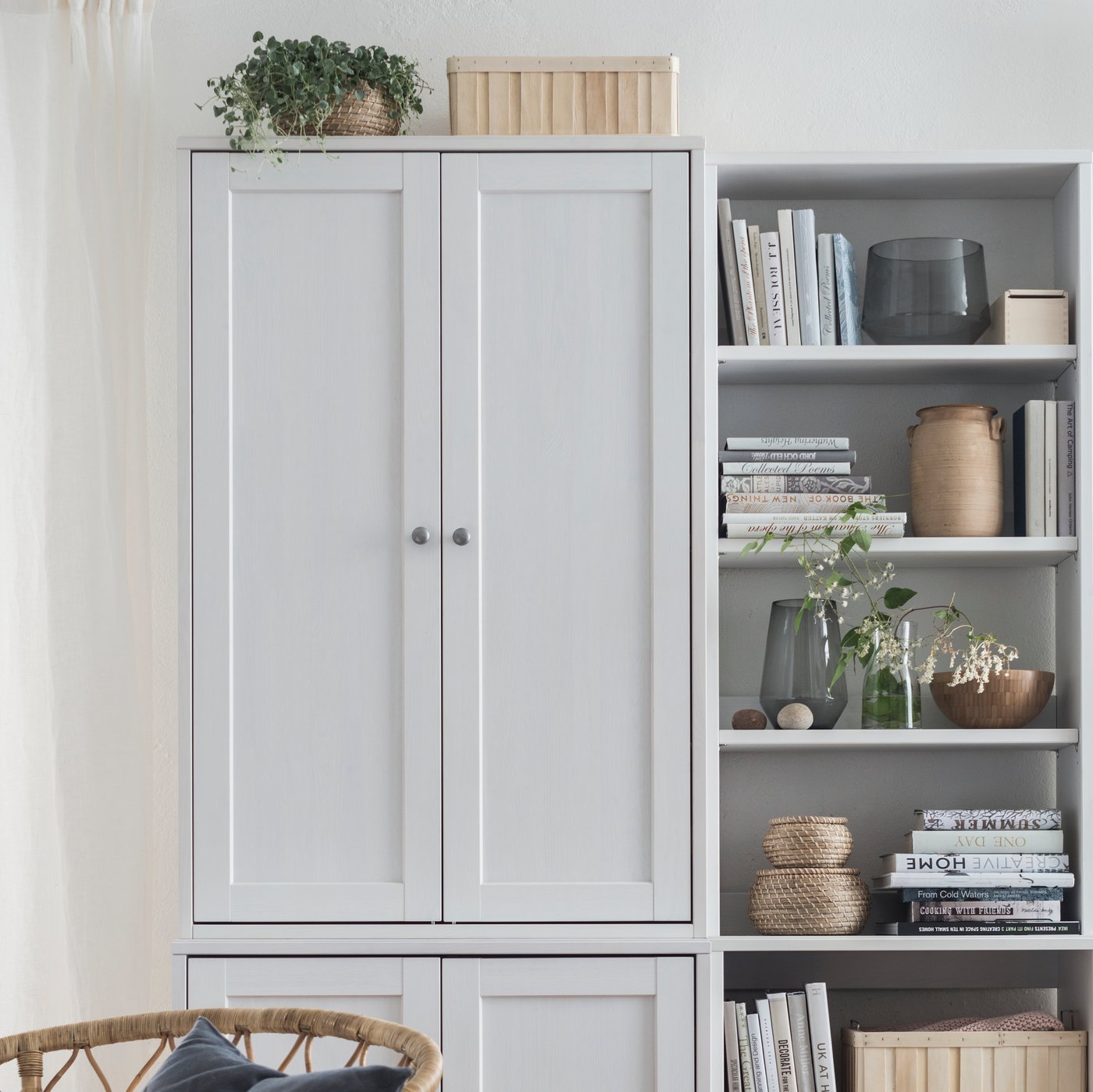 Un rangement avec portes HAVSTA à côté d’une étagère ouverte avec plinthe HAVSTA, derrière un fauteuil en rotin.