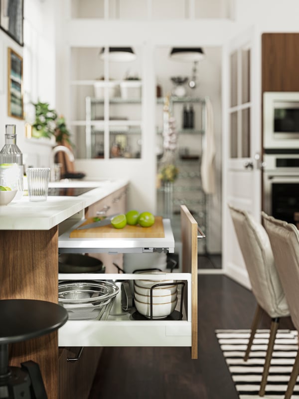 Una cocina con una superficie de trabajo extraíble UTRUSTA abierta en primer plano y una despensa y varios electrodomésticos de fondo.