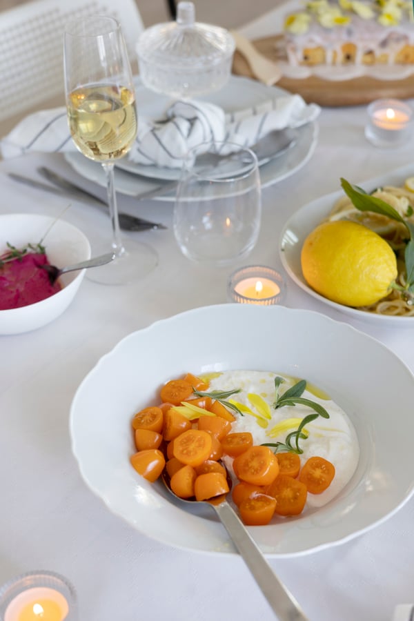 Burrata med tomater anrettet på en tallerken på et opdækket bord.