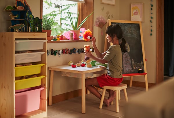 Niña sentada en su escritorio de madera haciendo manualidades. Al costado izquierdo se ve un mueble TROFAST con juguetes encima.