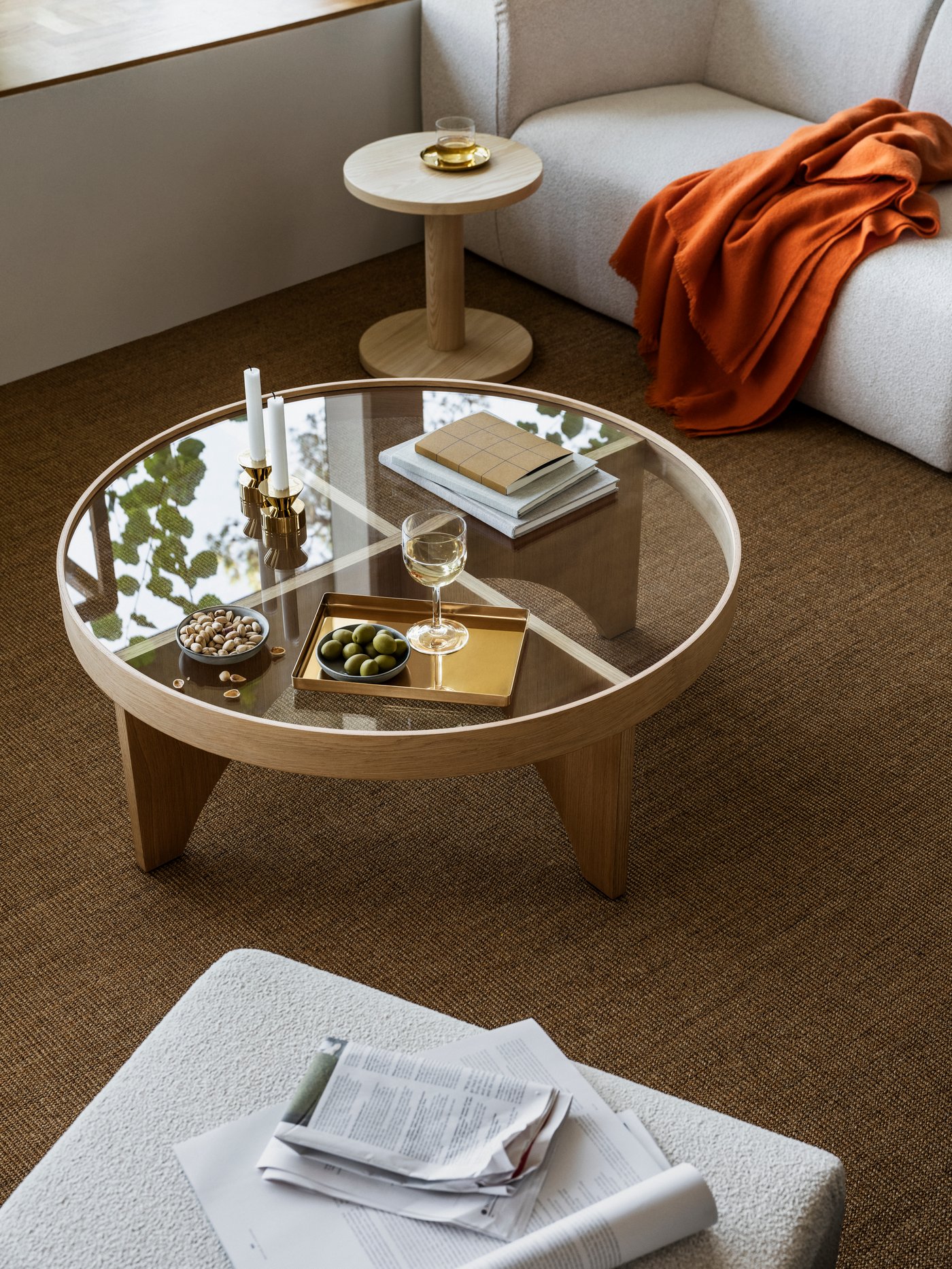 A brass-coloured tray on a STOCKHOLM 2025 coffee table in oak veneer and glass placed next to a pine veneer side table.