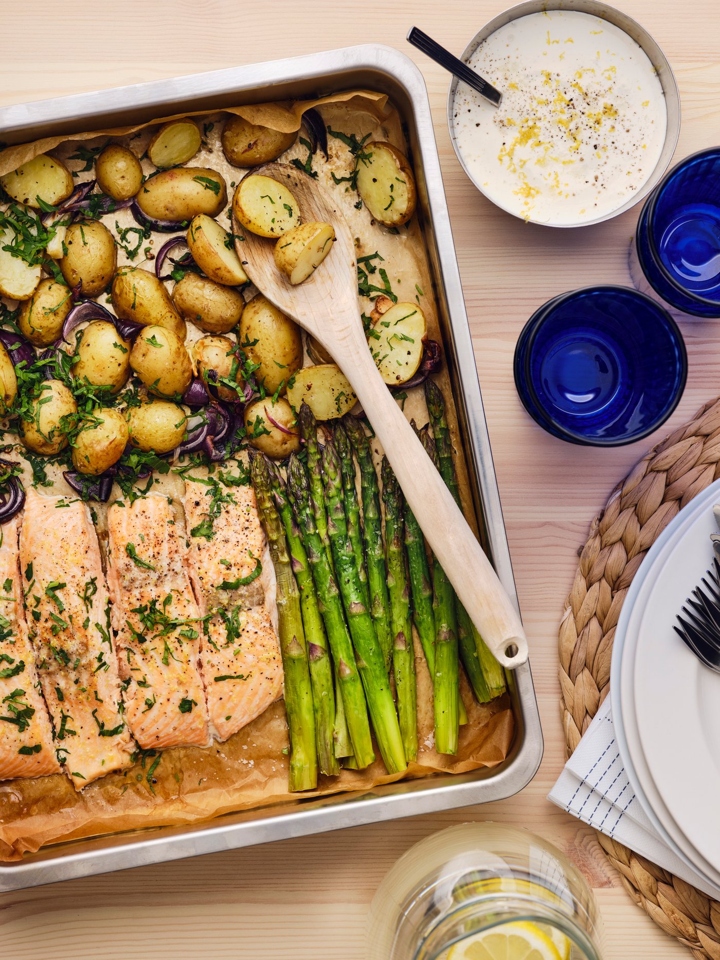 Roasted salmon, baby potatoes, asparagus, and lemon sauce served on a tray with plates, glasses, and a pitcher.