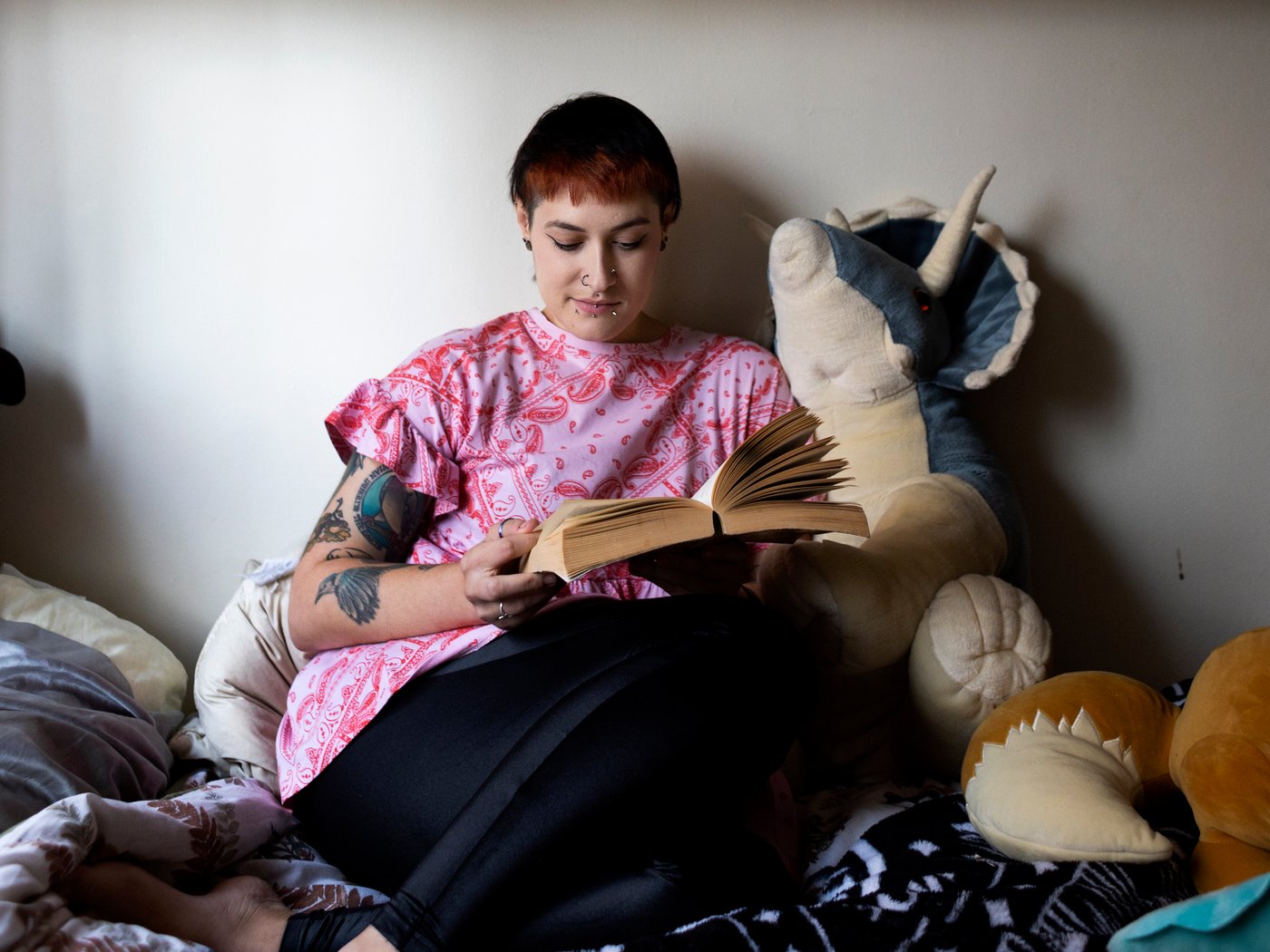 Woman sitting on her bed, surrounded by soft toys, reading a big book.