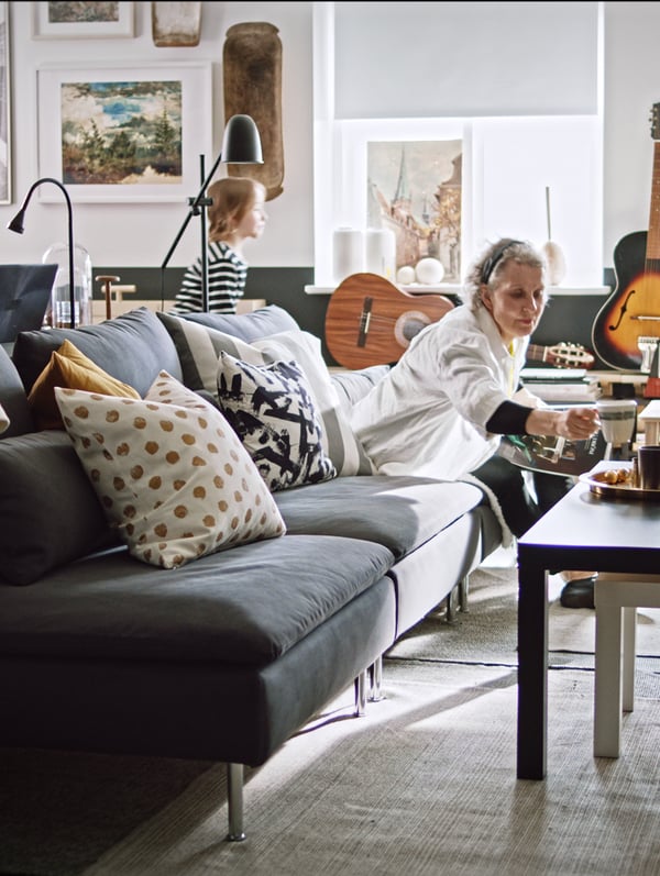 A grey SÖDERHAMN sofa with a lady sitting on it, leaning towards a coffee table with food on it.