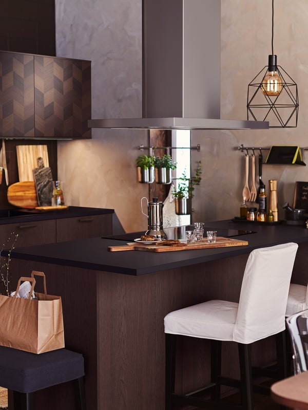 A kitchen with a BERGMUND bar stool, a kitchen island with various items and a black BRUNSTA pendant lamp and bulb.