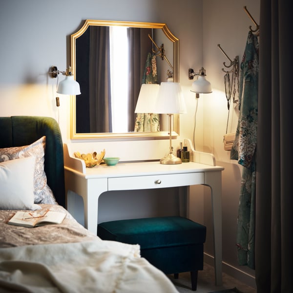 Bureau LOMMARP beige clair dans un angle, sous un miroir SVANSELE et près d’un lit matelassé TUFJORD en vert foncé.