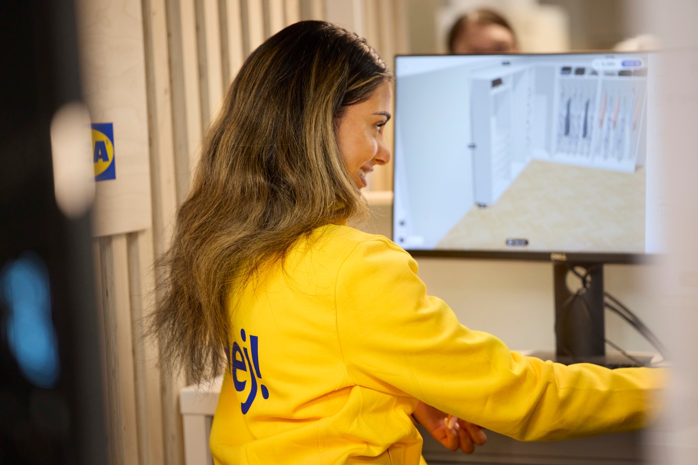 Ein:e IKEA Mitarbeiter:in lächelt vor einem Bildschirm mit einer 3-D-Skizze.