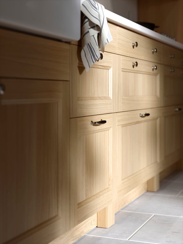 A row of VEDHAMN oak drawer fronts in a kitchen with a white marble effect worktop above them and white tiles on the floor.