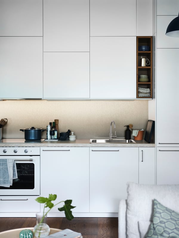 An open plan white METOD kitchen with a beige stone effect/laminate SÄLJAN worktop and a white MATTRADITION forced air oven.