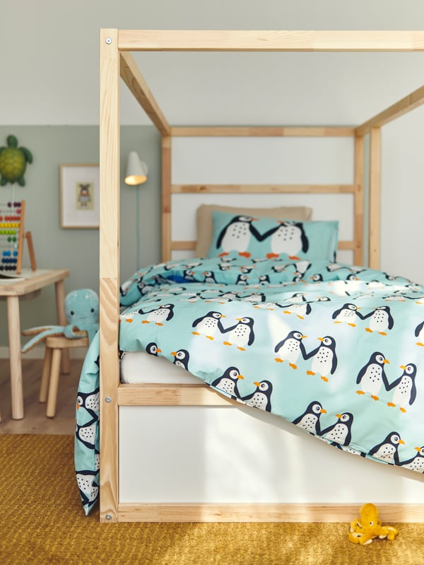 A KURA reversible bed with BLÅVINGAD bed linen with a penguin pattern stands in a bedroom on a yellow LANGSTED rug.
