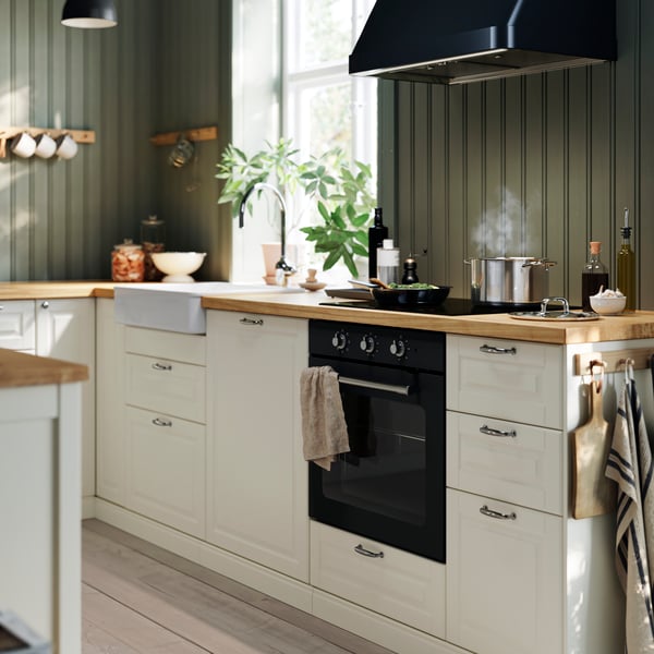 
A kitchen in a traditional style featuring BODBYN kitchen doors in off-white, wooden flooring, and green walls with wooden paneling.