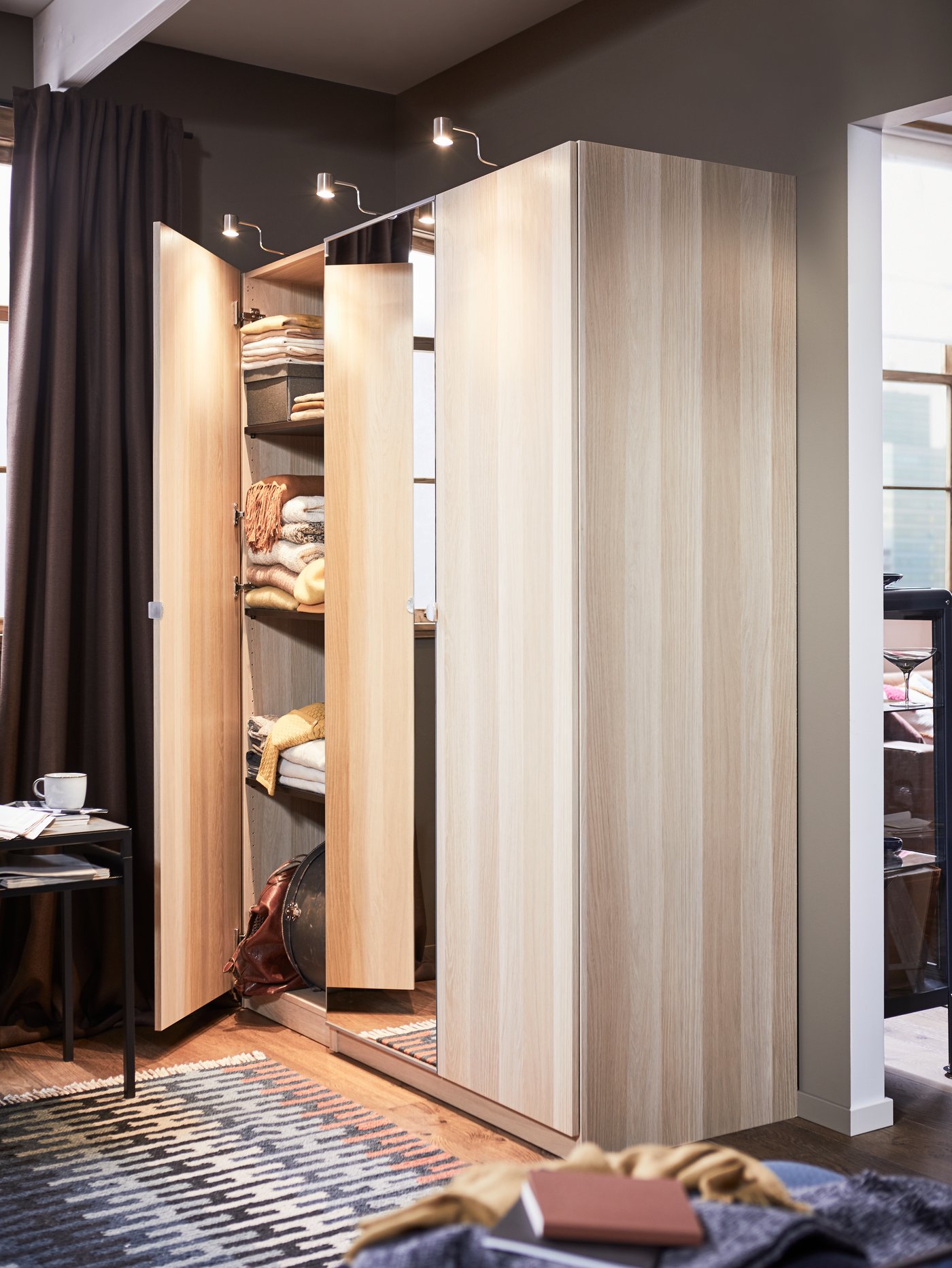 A PAX wardrobe system with one door open revealing folded clothing on shelves inside.