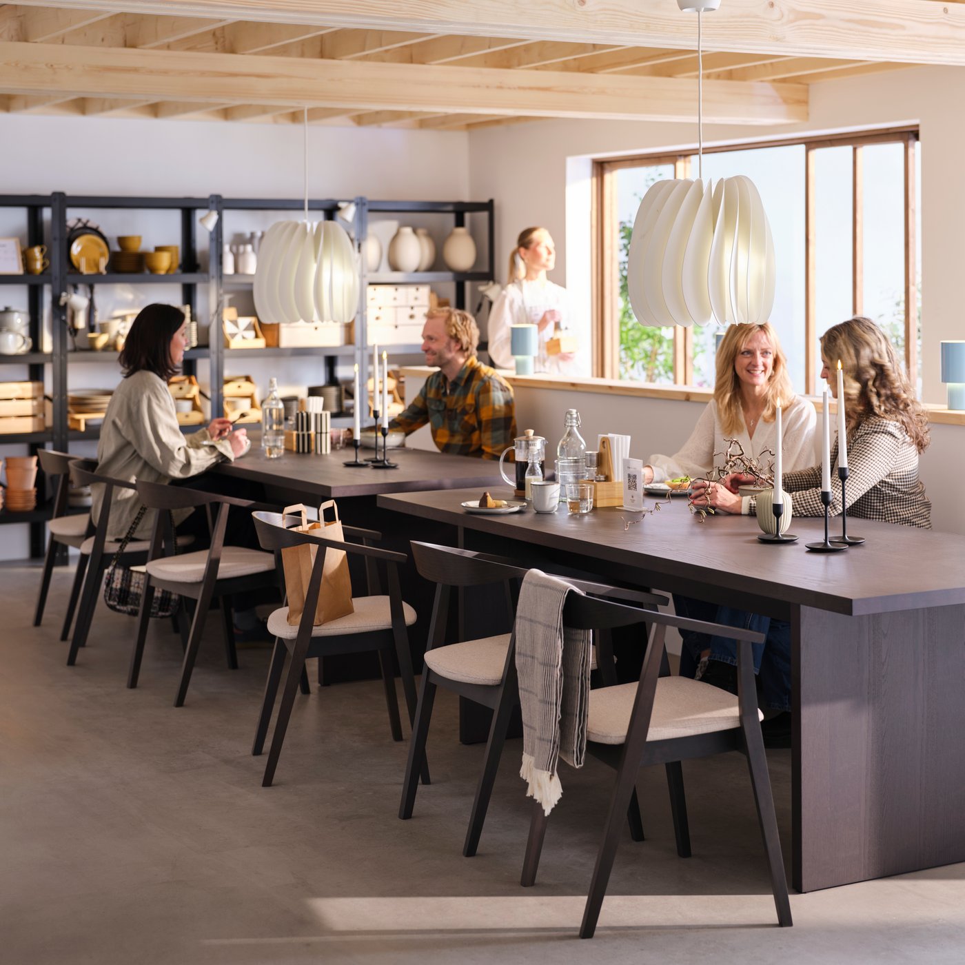 Several people sitting on STOCKHOLM chairs at BERGSHYTTAN tables in the light and spacious café section of a pottery shop.