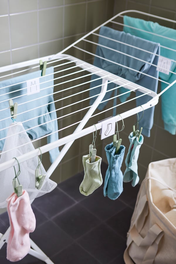 Gros plan sur un séchoir MULIG où des vêtements et des chaussettes de couleur sont suspendus à l’aide de pinces à linge SLIBB.
