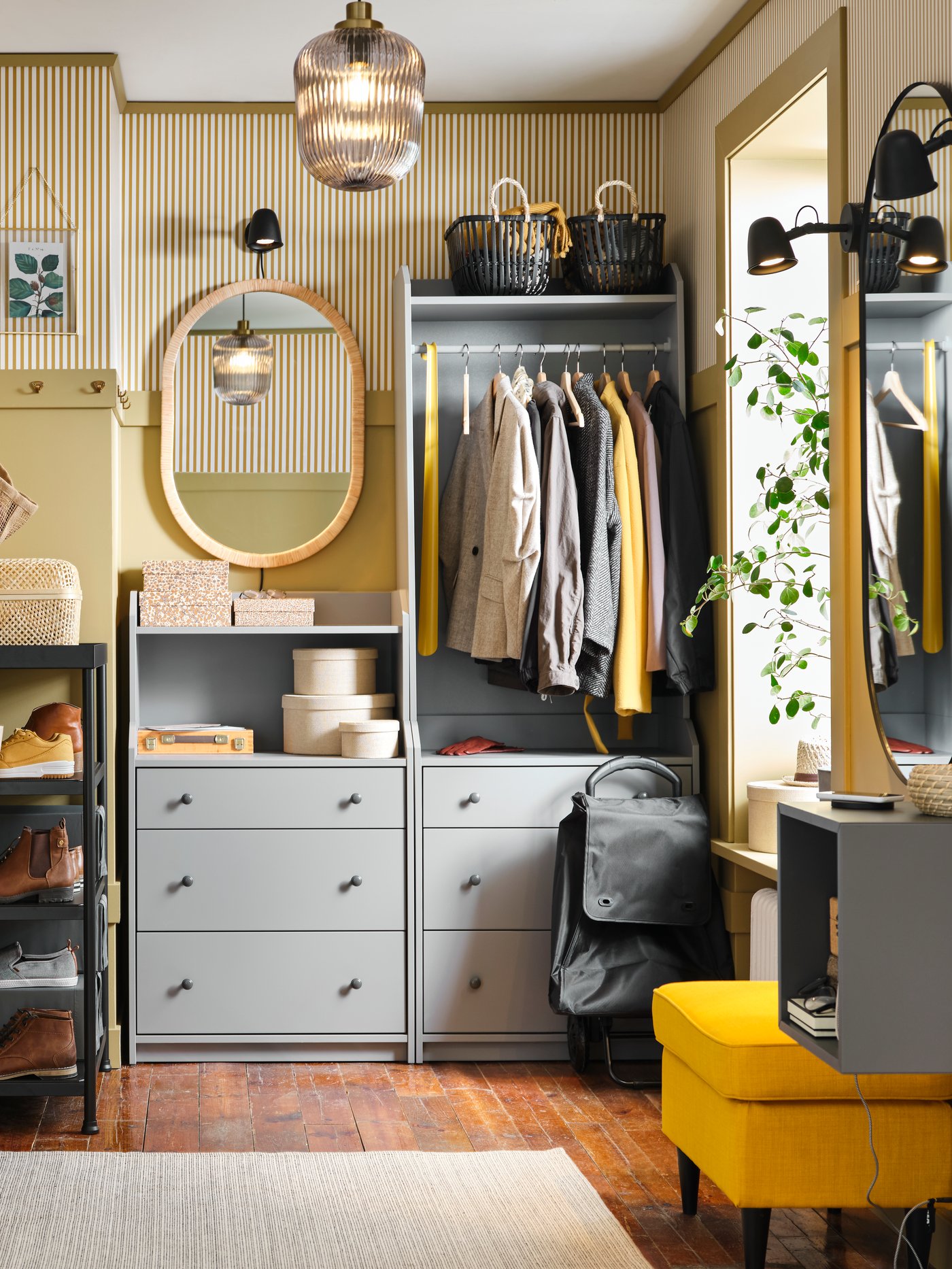 A stylish and organized entryway with a grey HAUGA open wardrobe, a vibrant yellow ottoman, and yellow-striped wallpaper, creating a warm and eclectic feel.