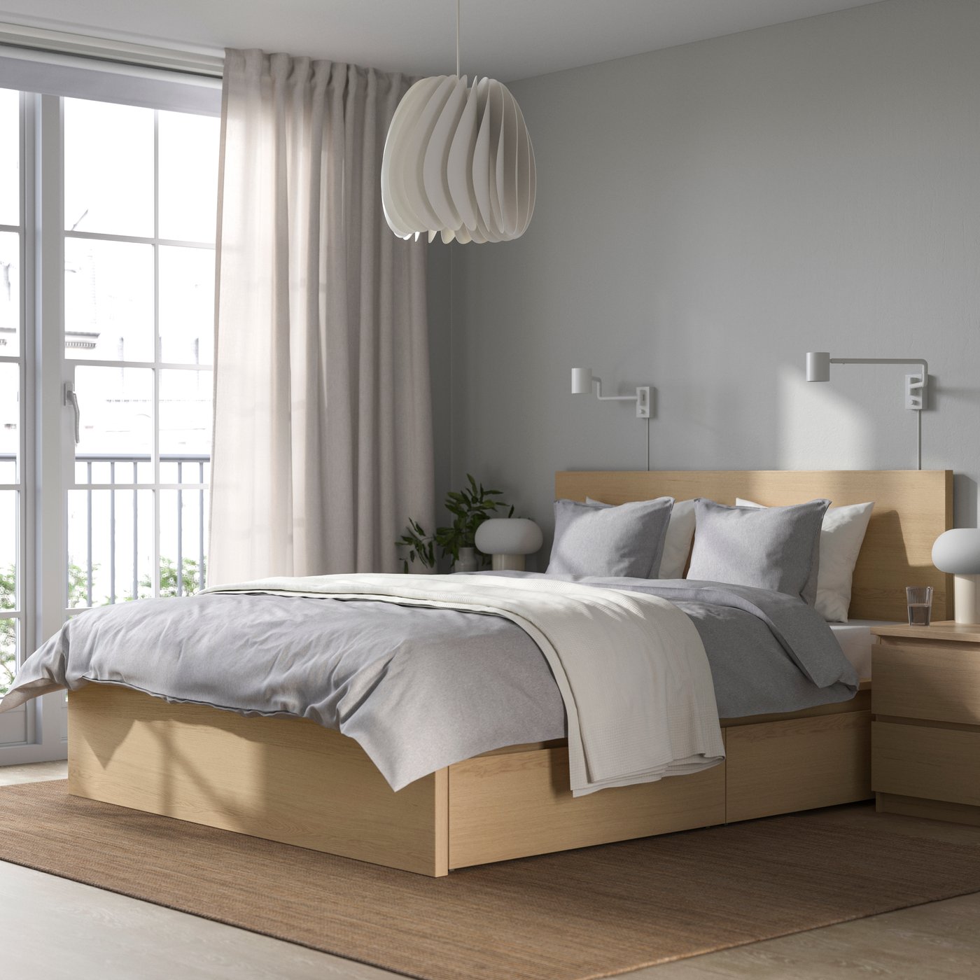 Cama MALM de madera con sopa de cama gris. Sobra la cama una manta blanca. Al costado de la cama una gran ventana con ortinas  medio cerrar que dejan entrar el sol.
