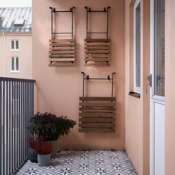 Une table TÄRNÖ pliée et deux chaises TÄRNÖ pliées sont suspendues allumé un mur allumé un balcon, près de quelques plantes en pot.