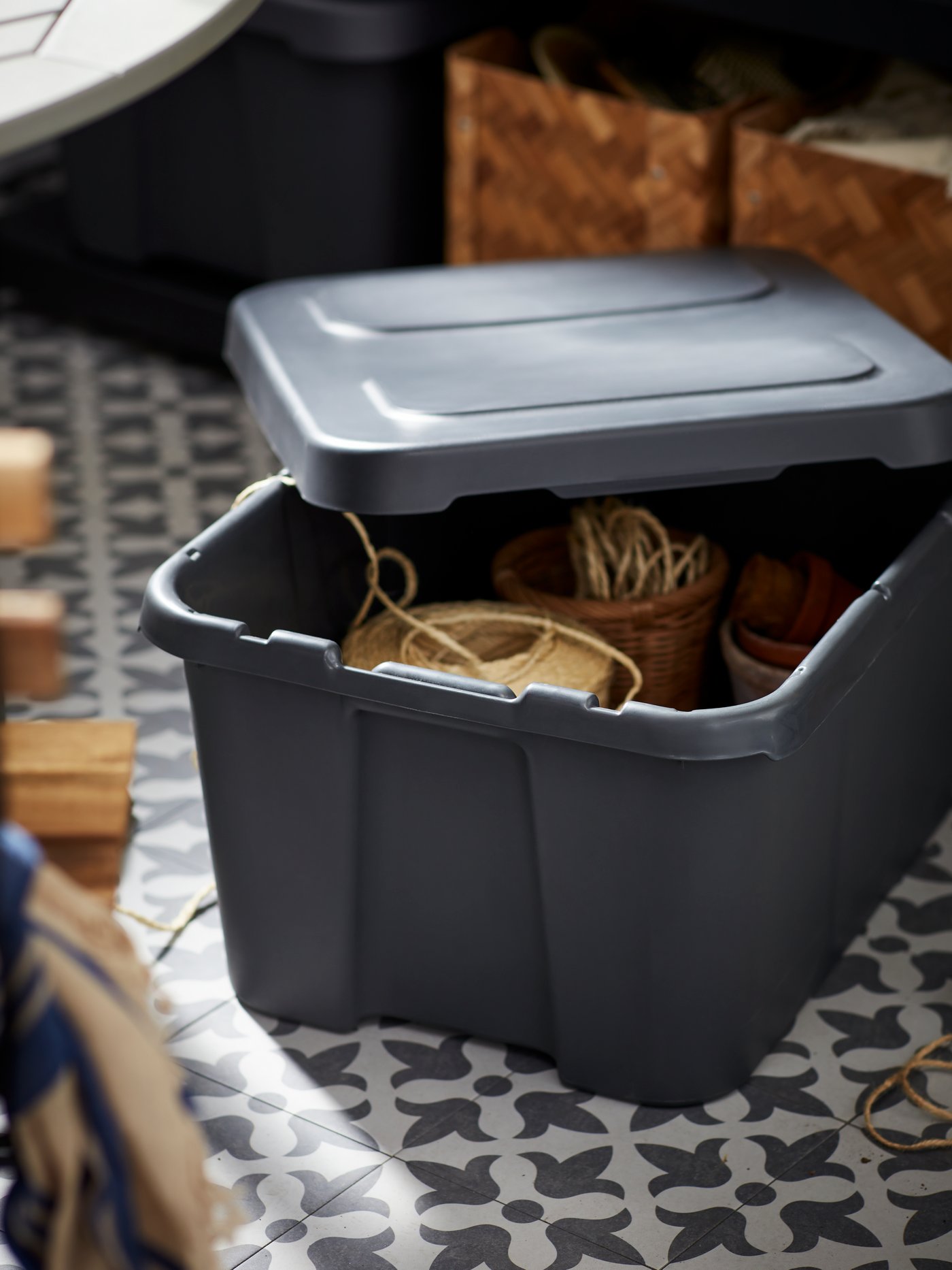 Plastförvaringslåda med lock fylld med föremål placerad på golv i garage, anpassad för fuktiga och kalla utrymmen.