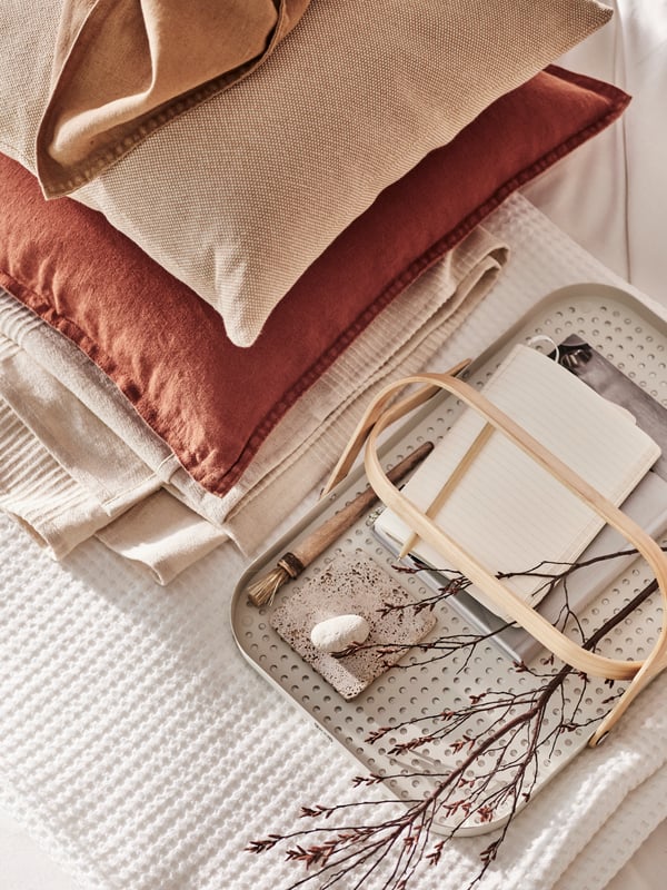 Two cushions, one in a red-brown DYTÅG cover and the other in a pink SANDTRAV cover in a pile with other folded bed linen.