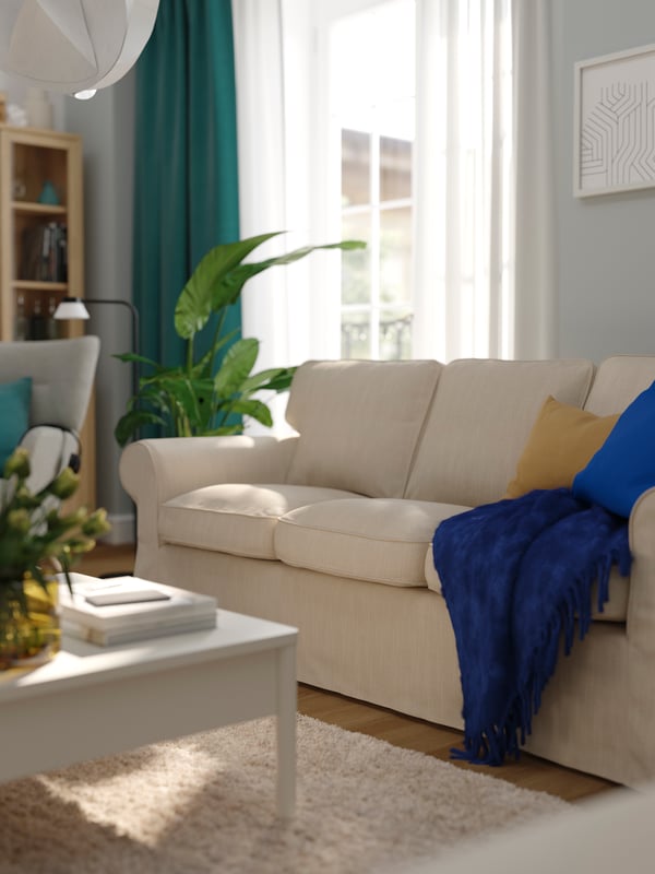 An EKTORP sofa, with a throw and some extra cushions on it, stands in a living room near a large window.