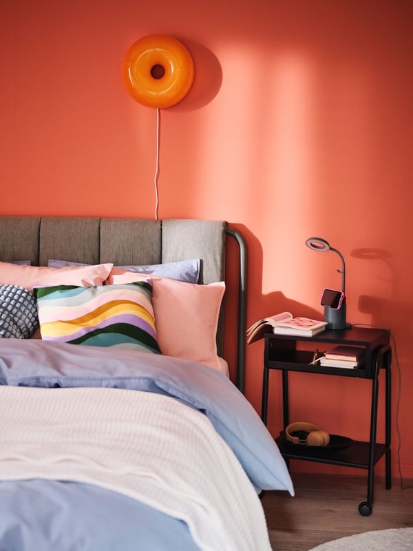Lit matelassé TÄLLÅSEN avec linge de lit ÄNGSLILJA gris bleu posé dessus. Lampe de table/applique à DEL VARMBLIXT fixée au mur.