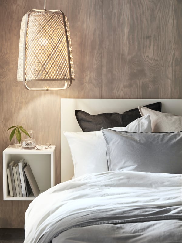 A bamboo/handmade KNIXHULT pendant lamp in the bedroom above a small hanging EKET bedside table next to a bed