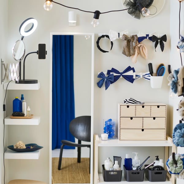 Une mini-commode MOPPE en bouleau contreplaqué sur une tablette blanche avec accessoires pour cheveux sur le dessus, à côté d’un miroir NISSEDAL blanc sur le mur.
