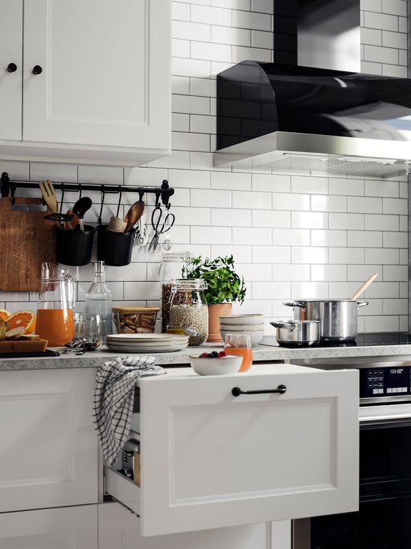 AXSTAD matte white kitchen cabinet doors with a drawer partially open, and a countertop set with juice, a bowl of fruit.