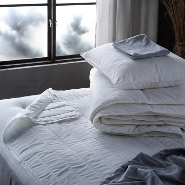 Bed with a LUDDROS mattress protector, and a SMASPORRE duvet folded neatly with a VILDKORN pillow on top. 