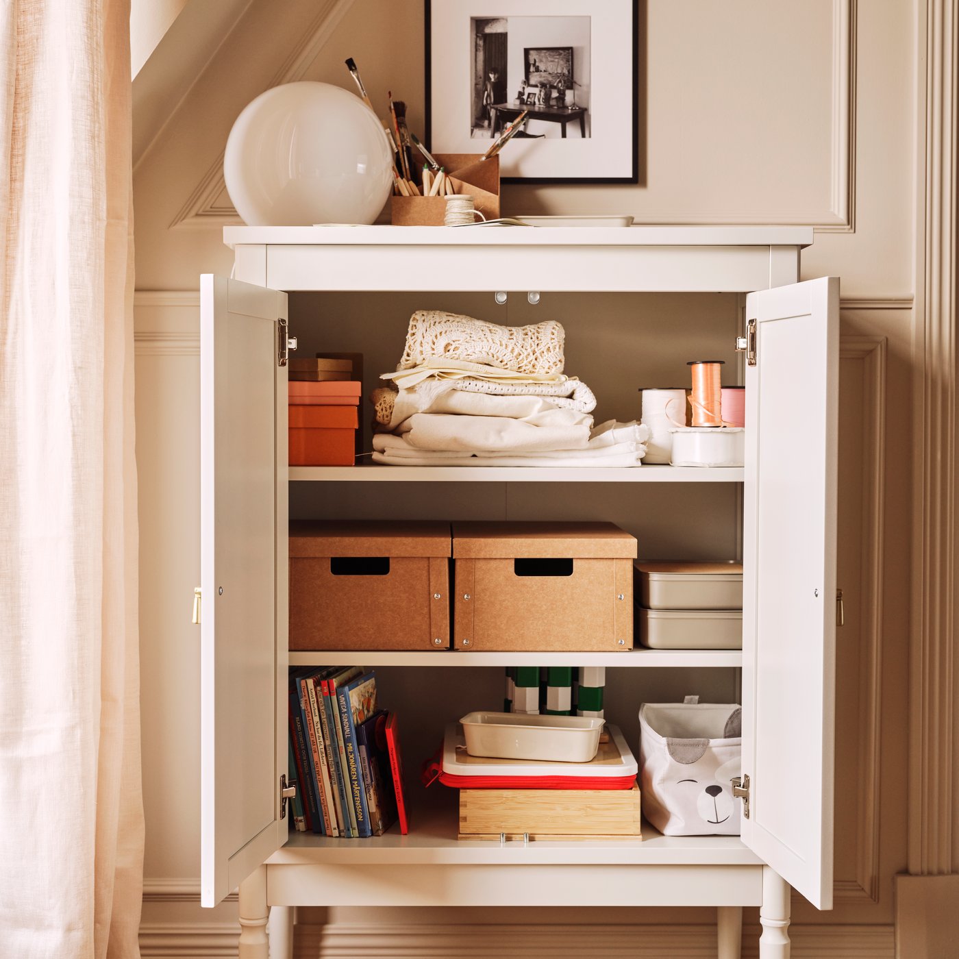 An off-white FÄRJKARL cabinet with many things on its shelves including two GÄRDESGÅRD storage boxes and a DRÖMSLOTT box.