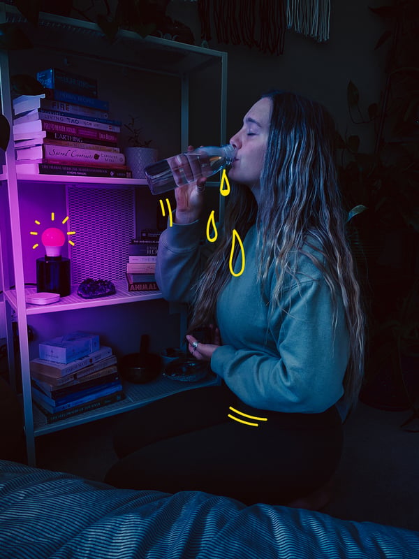A woman taking a sip of water while sitting in front of a purple light.