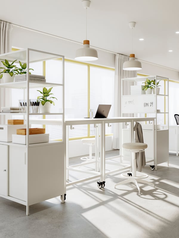 A workspace formed by a combination of white TROTTEN frames and cabinets beneath beige-and-birch BUNKEFLO pendants.